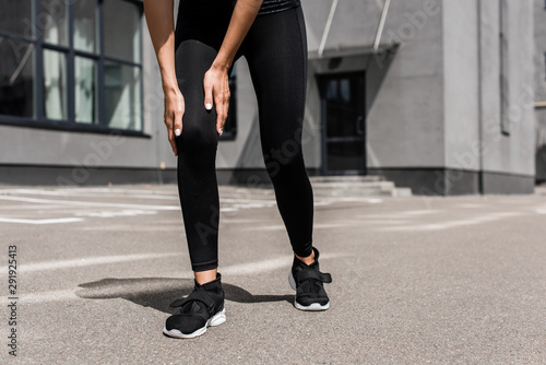 cropped view of sportswoman in black sneakers with knee pain on street