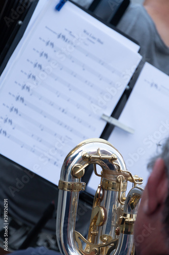 Cropped image of a back turned saxophone player. In the background, an out of focus score