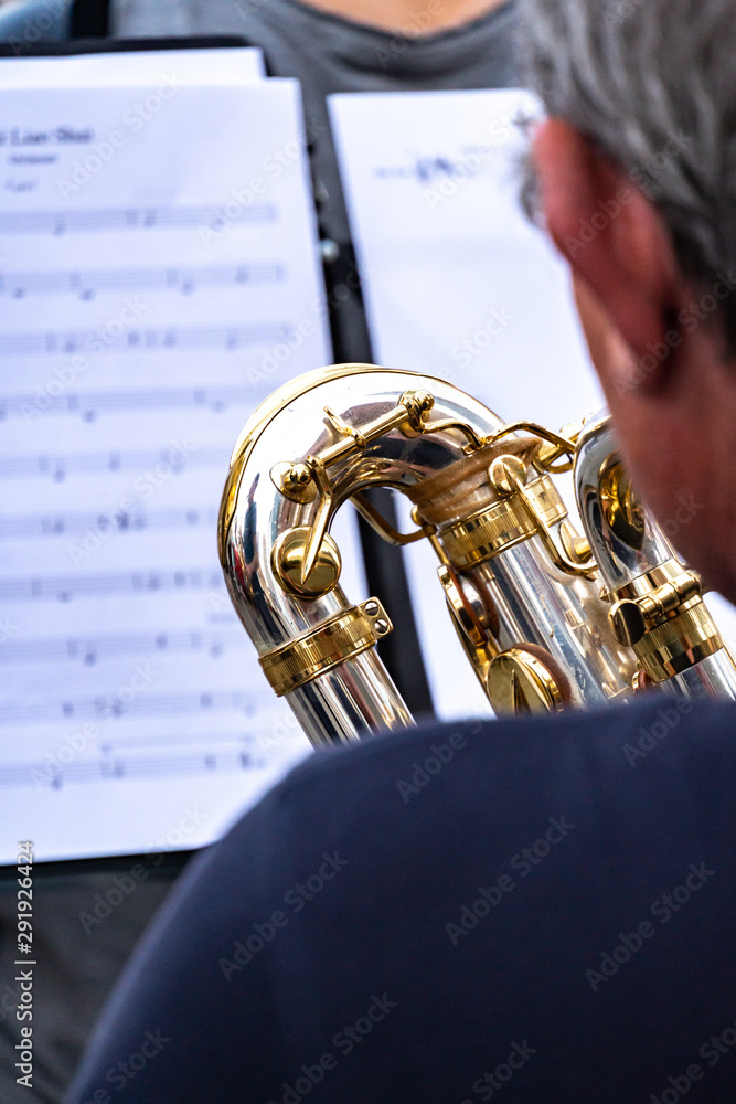 Obraz premium Cropped image of a back turned saxophone player. In the background, an out of focus score