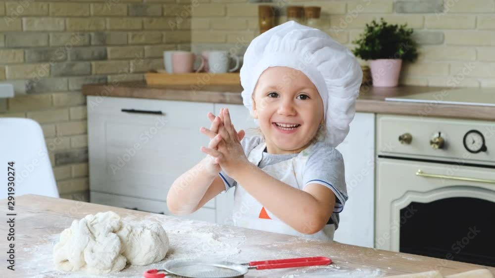 Happy baby girl in the kitchen playing with flour to have fun. A child dressed as a cook. 4K video. Happy baby girl in the kitchen playing with flour to have fun. A child dressed as a cook. 4K video.