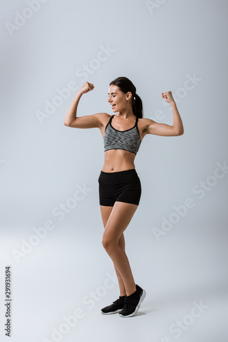 full length view of smiling sportswoman on grey