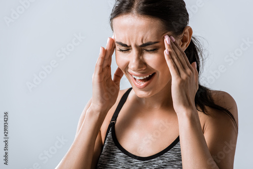 attractive sportswoman with headache touching temples isolated on grey