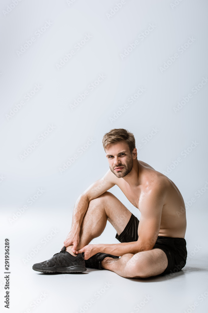 shirtless bearded sportsman with ankle pain on grey shirtless bearded sportsman with ankle pain on grey