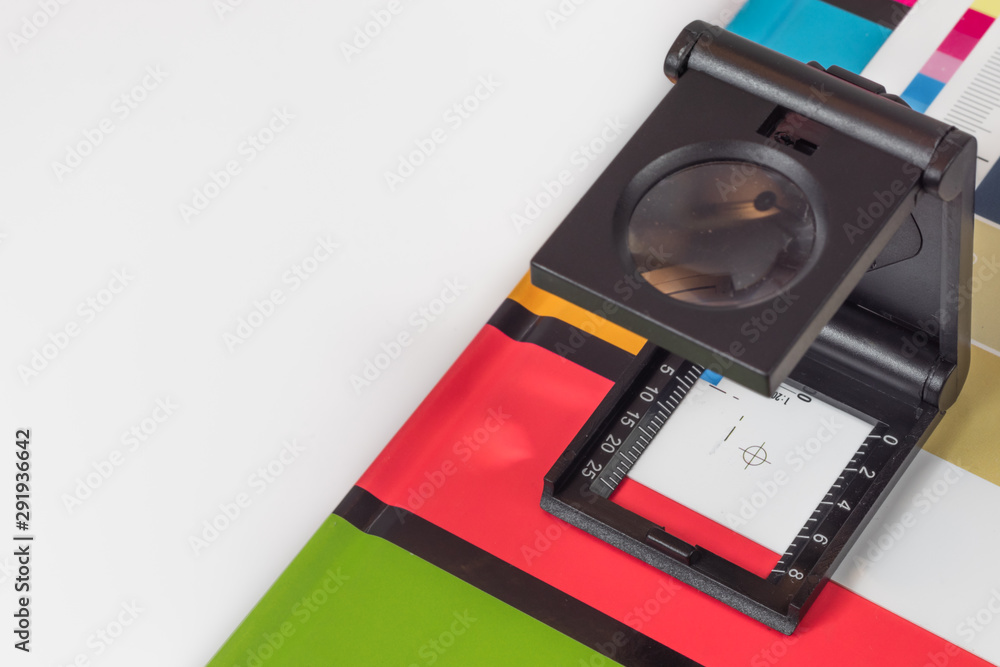 Fototapeta premium Black magnifying glass standing on the test print with colored background. Print loupe on offset printed sheet with basic colors control bars.