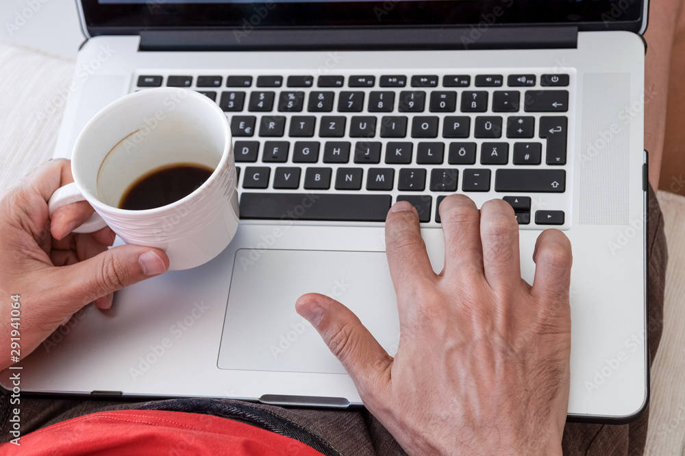 Male freelancer using laptop touchpad while enjoying cup of coffee at home Male freelancer using laptop touchpad while enjoying cup of coffee at home