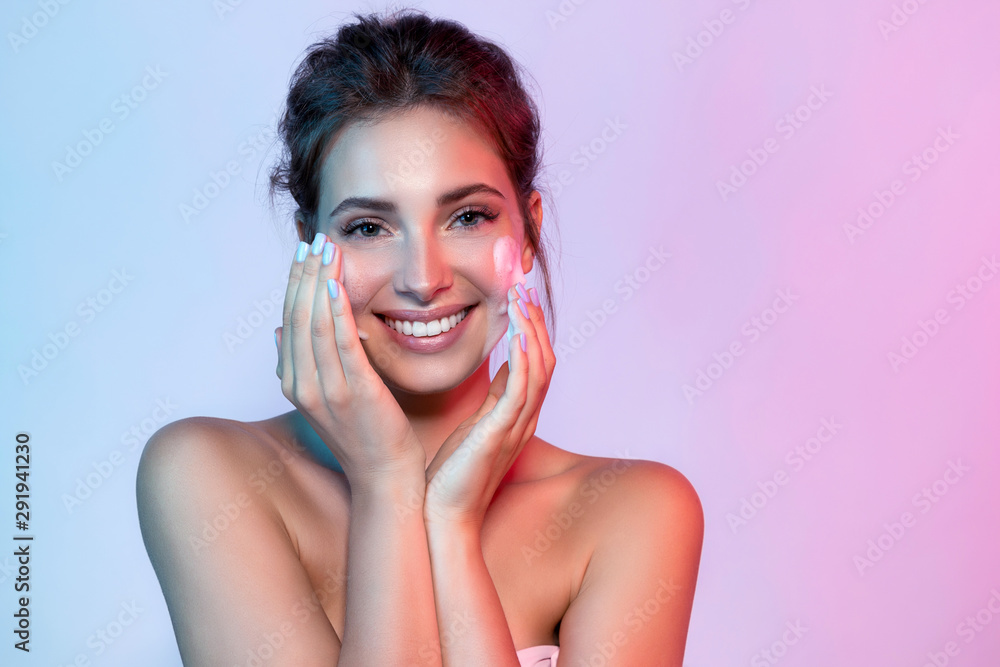 Portrait of beautiful woman applying skin cleansing foam and looking at camera with joyfulness. Wonderful young model using facial moisturizing cosmetic. Beauty and clean skin concept - obrazy, fototapety, plakaty 