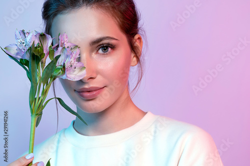 Portrait of beautiful woman closing half of face by spring flower. Beautiful lady with perfect clean skin and natural make-up looking at camera with happiness. Beauty and fashion concept