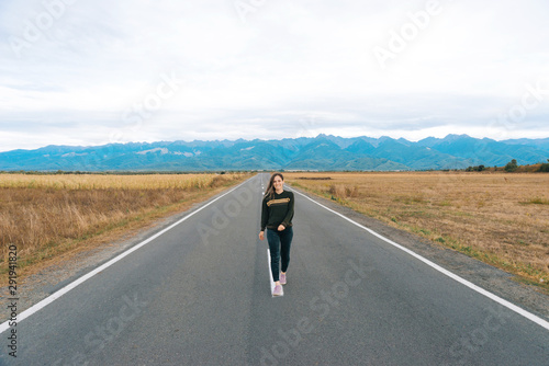 Photo of beautiful young woman enjoying free time in mountains, standing in middle of the road