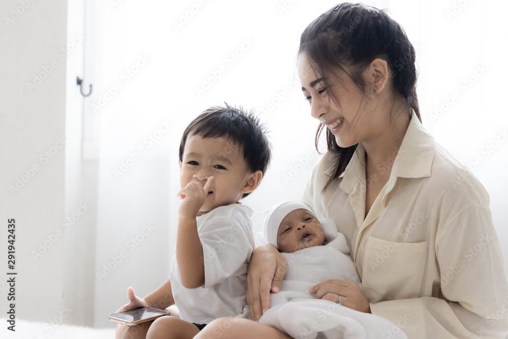 Young Asian mother hugging a cute newborn baby and feeding milk form bottle in with the son white bedroom. Duty of the wife to raise children. Mother and child concept Young Asian mother hugging a cute newborn baby and feeding milk form bottle in with the son white bedroom. Duty of the wife to raise children. Mother and child concept