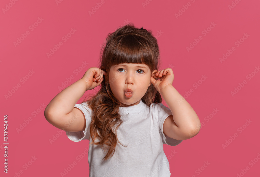 Close-up portrait of a little brunette girl dressed in a white t-shirt posing against a pink studio background. Sincere emotions concept. Close-up portrait of a little brunette girl dressed in a white t-shirt posing against a pink studio background. Sincere emotions concept.