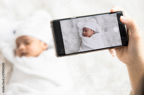 Mother 's hand holding smartphone use to taking photo cute newborn baby for memories and pose in social network.