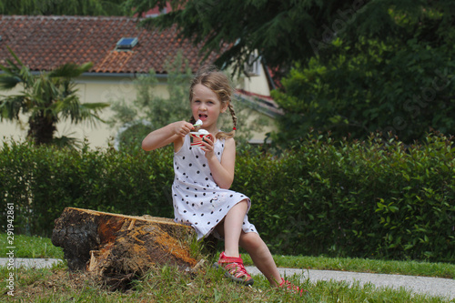 Little blonde girl eating ice cream with a spoon from a paper cup