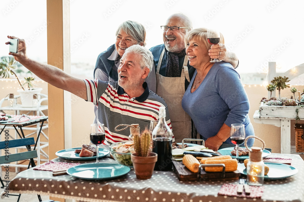 Happy seniors friends taking selfie with mobile smartphone camera at dinner on terrace - Retired people having fun eating and drinking red wine on patio while using new trends technology phone apps Happy seniors friends taking selfie with mobile smartphone camera at dinner on terrace - Retired people having fun eating and drinking red wine on patio while using new trends technology phone apps