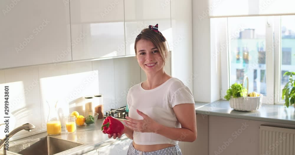 Portrait of the young Caucasian pretty woman housewife standing in the kitchen, playing with a red paper in hand and smiling to the camera.