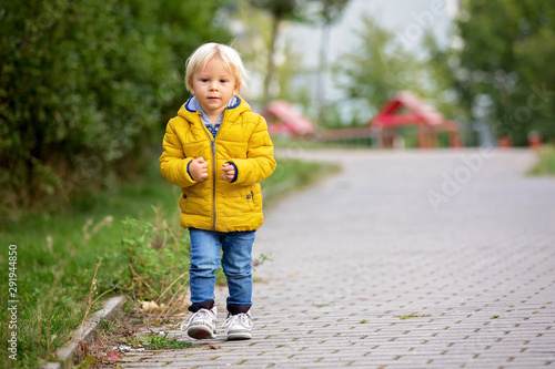 Blonde little toddler child in yellow jacket, playing on the playground