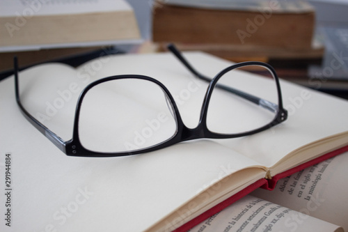 Close up glassess on blank red notebook and history book with old books in background. Education and reading concept
