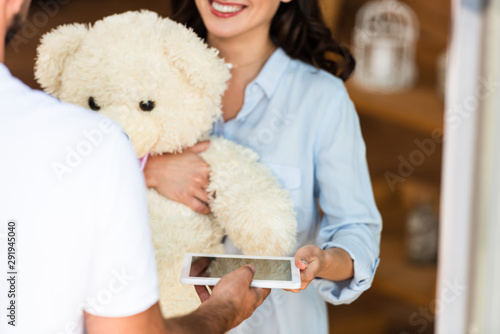 cropped view of delivery man holding digital tablet near happy woman with teddy bear