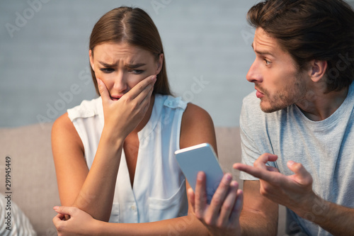 Husband Showing Cheating Wife Her Phone Sitting On Sofa Indoor photo