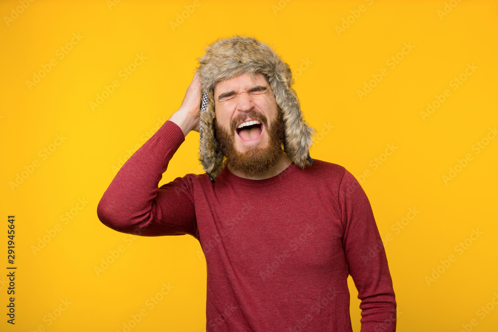 Photo of young bearded man screaming over yellow background in winter hat Photo of young bearded man screaming over yellow background in winter hat