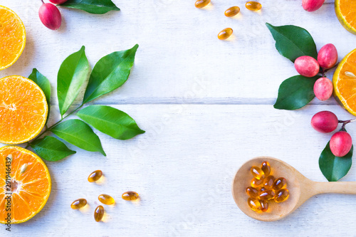 Vitamin supplements on wooden spoon with healthy fruit orange and Koronda Fruit (wild berries) with green leaf on white wooden background.Top view.