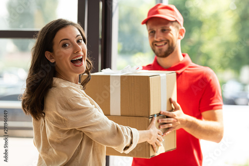 selective focus of happy woman receiving carton boxes from cheerful delivery man in cap photo