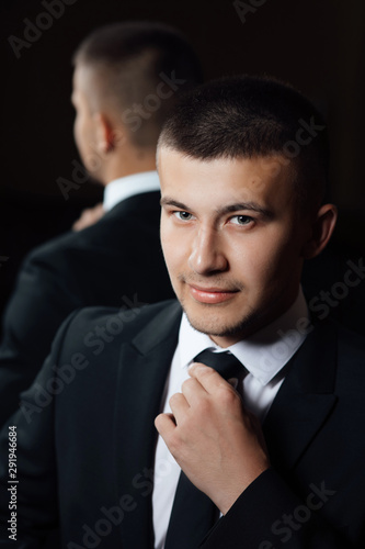 Happy groom straightens his tie. Portrait of a young man. Morning groom. Groom getting ready in the room for wed day.