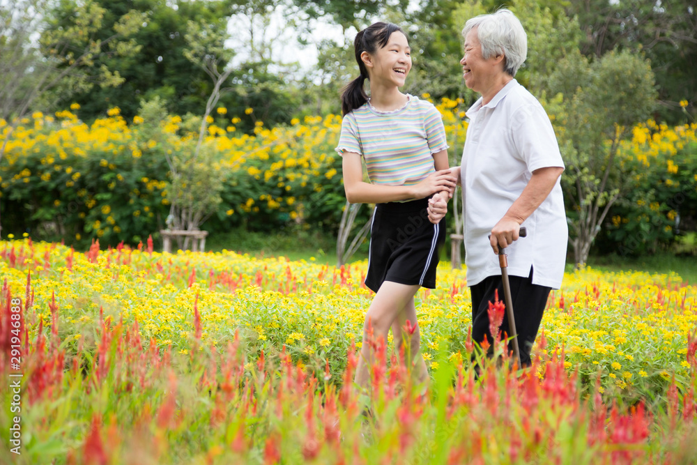 Happy asian senior grandmother and granddaughter walking in blooming garden,simple stress reduction,enjoying nature,smiling child girl holding hand of elderly woman care,support,health care concept - obrazy, fototapety, plakaty 