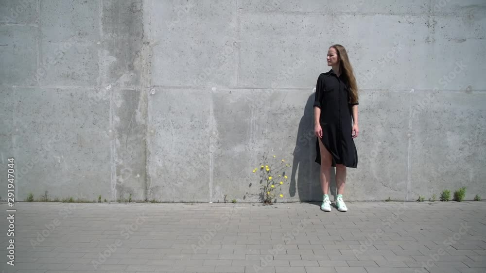 A slender fair-skinned girl with blond long hair in a black dress stands alone in the industrial zone A slender fair-skinned girl with blond long hair in a black dress stands alone in the industrial zone