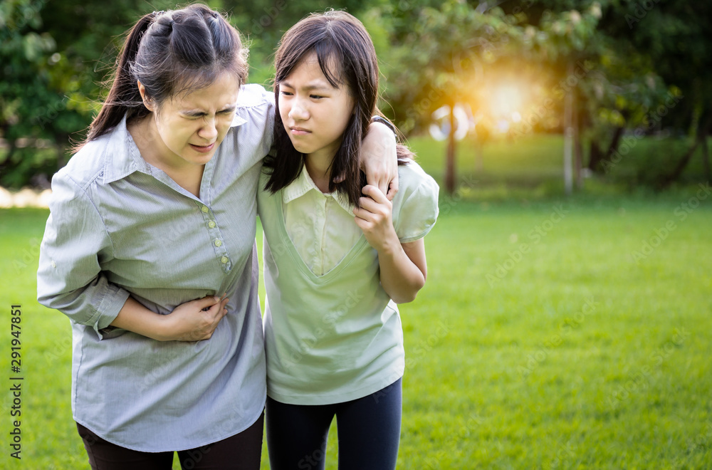 Asian woman touching stomach painful with daughter, child girl help care support her mother suffer from stomachache,symptoms gastrointestinal system disease,problems with the gut and digestion Asian woman touching stomach painful with daughter, child girl help care support her mother suffer from stomachache,symptoms gastrointestinal system disease,problems with the gut and digestion