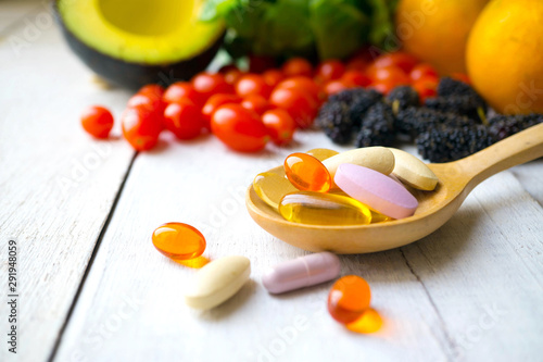 Pills and capsules in wooden spoon with fresh fruits.Vitamins and supplement from fruits concept.