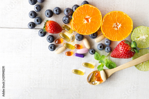 Multivitamins and supplements with fresh and healthy fruits on white wooden background. photo