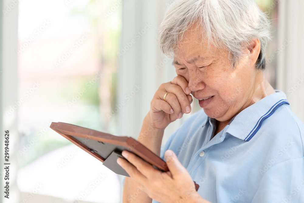 Depressed asian senior holding a picture frame and watching old photographs of family at home, elderly people crying,moaning over an old photograph of her husband and son,missing lover,loneliness Depressed asian senior holding a picture frame and watching old photographs of family at home, elderly people crying,moaning over an old photograph of her husband and son,missing lover,loneliness