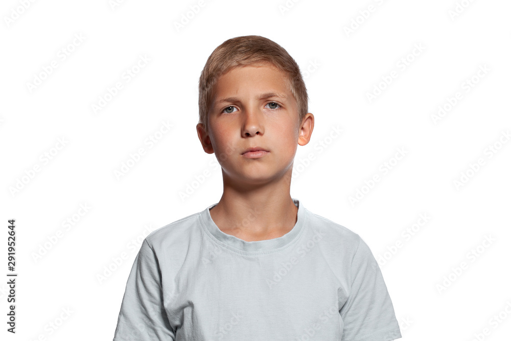 Close-up portrait of a blonde teenage boy in a white t-shirt posing isolated on white studio background. Concept of sincere emotions.
