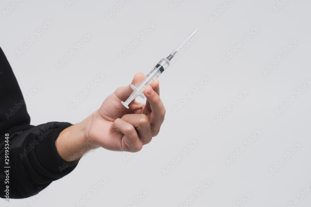 Man's hand hold a syringe with liquid. Guy in a black hoodie on a white background. Person offers you drug or medical treatment. Drug addict. Dangerous self-medication. Copy space. Man's hand hold a syringe with liquid. Guy in a black hoodie on a white background. Person offers you drug or medical treatment. Drug addict. Dangerous self-medication. Copy space.