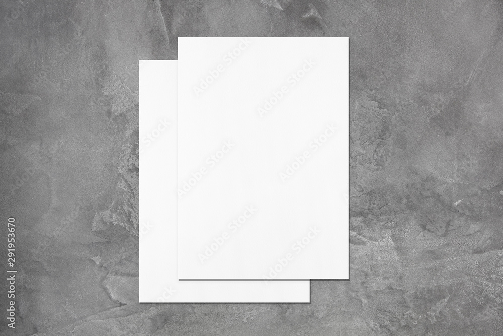 Two empty white rectangle poster mockups lying on top of each other with soft shadows on dark grey concrete background. Flat lay, top view Two empty white rectangle poster mockups lying on top of each other with soft shadows on dark grey concrete background. Flat lay, top view