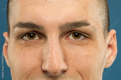 Caucasian young man's close up shot on blue studio background. Beautiful model with well-kept skin. Concept of human emotions, facial expression, male beauty and healthcare. Eyes calm and eyebrow.