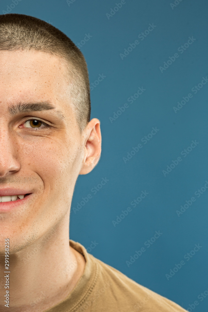 Obraz premium Caucasian young man's close up shot on blue studio background. Beautiful male model in shirt. Concept of human emotions, facial expression, sales, ad. Smiling, looks happy.