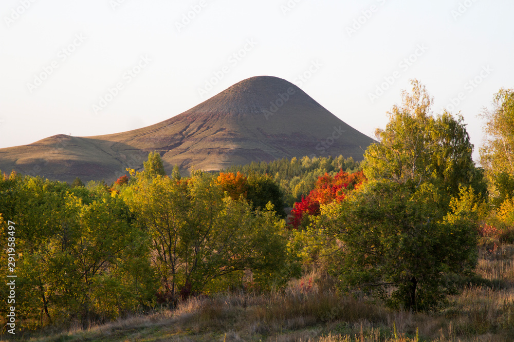 Fototapeta premium A single mountain surrounded by deciduous and coniferous trees.