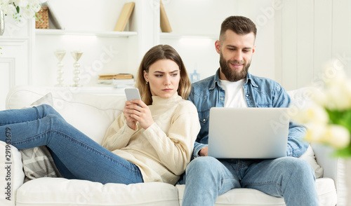 Woman looking at husband's laptop, sitting together on sofa