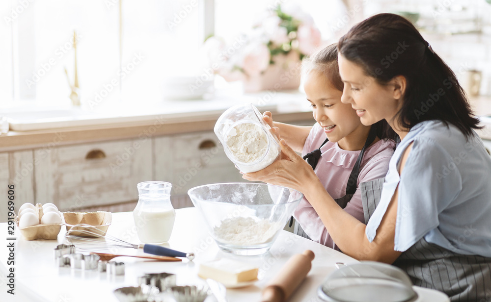 Mother and daughter preparing dough for bake cookies, adding flour to bowl Mother and daughter preparing dough for bake cookies, adding flour to bowl