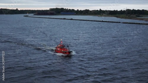 small red Riga pilot motorboat sails and accompanies tanker Onyx to raid at Daugava mouth under cloudy sky at twilight photo