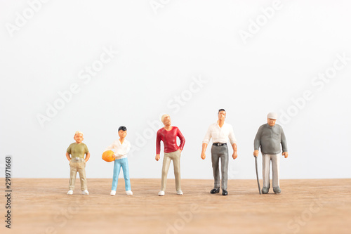 Miniature people in different ages stand on wood floor with white background