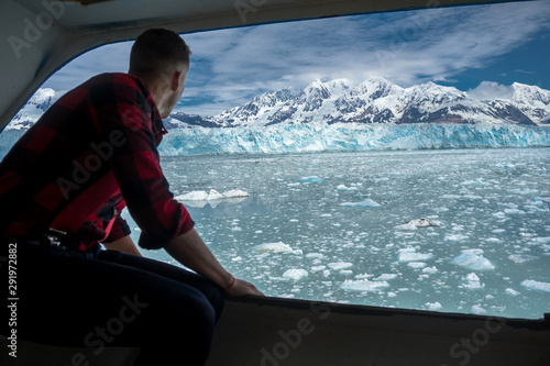 Young is looking on a beautiful Hubbard Glacier. He is on a cruise ship in Alaska. Gentleman is wearing a lumberjack shirt and watching the iceberg.