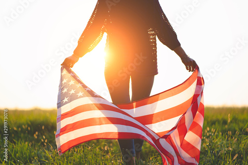 Patriotic woman with american flag outdoors at sunset. Travel to america and celebrate holiday of 4th of july in usa