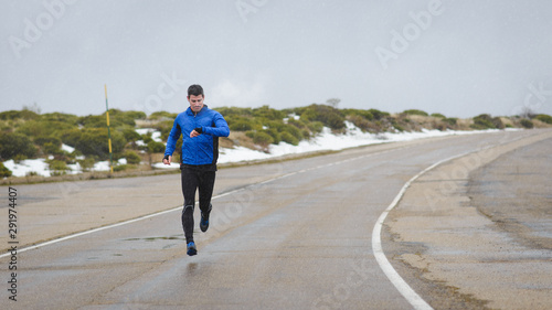 Full length athlete timing outdoor running workout on winter mountain road under the snow.
