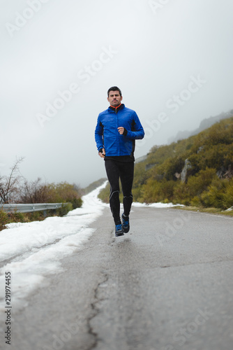 Athlete running under the snow on winter mountain road. Cold season outdoor training. © Dirima
