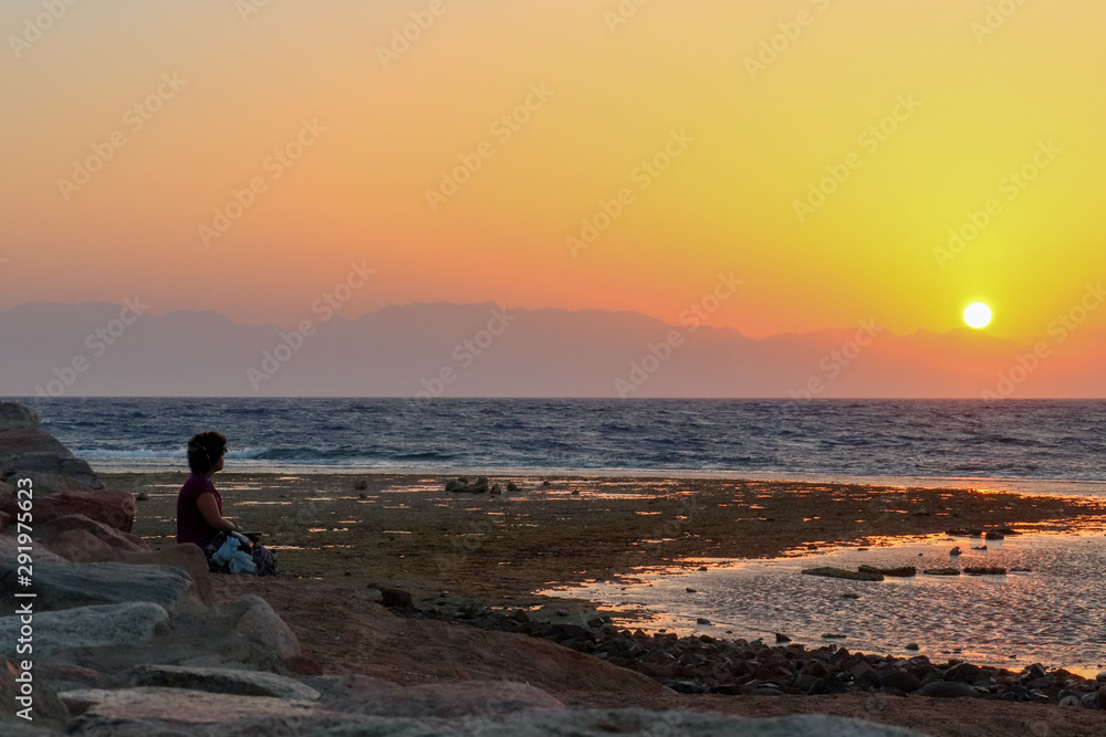 silhouette of a woman watching the sunrise by the coral reefs
