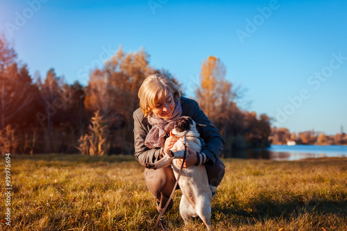 Walking pug dog in autumn park by river. Happy woman hugging pet and having fun with best friend.