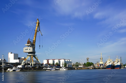 The seaport at the river Pregol with ships and cargo cranes on background of blue sky.