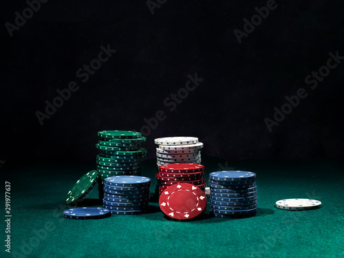 Close-up shot of a colorful chips piles, some of them laying nearby on green cover of playing table. Black background. Close-up. photo